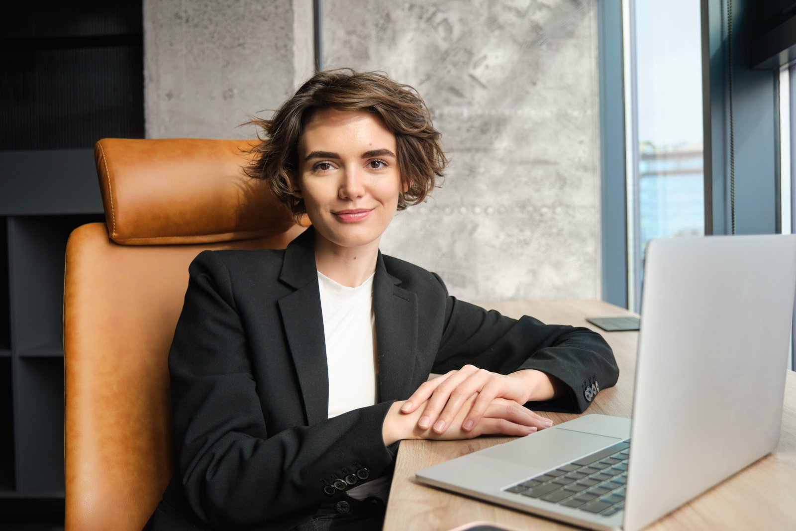 Businesswoman working on laptop, sitting in office in suit, waiting for client, preparing documentation for corporate meeting, using coworking space to focus on her work